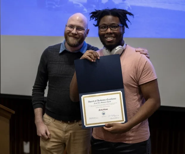 Professor Cole Denisen standing to the left of Nikh Glass holding his award.