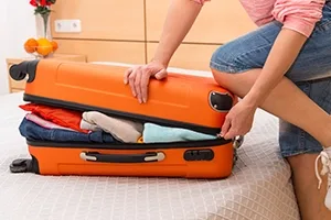 Someone kneeling on an overpacked orange suitcase.