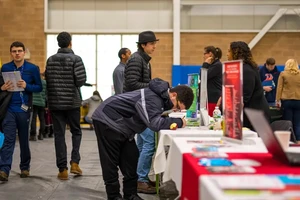 People interacting at the Landmark career fair with tables displaying brochures and posters.