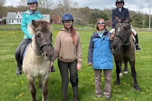 From left to right, Charlotte Graham, Olivia Arnell, Katherine Wagenbach '98, and Logan Lipschultz pose for a photo in a field. Charlotte and Logan are on horseback, while Olivia and Katherine are standing.