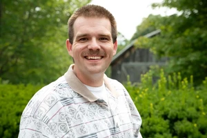 A photo of Professor Tyler Baker standing in front of a barn on the Landmark College campus.