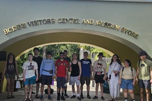 a group of students lined up under an archway with lettering that reads Bodine Visitors Center and Museum Store