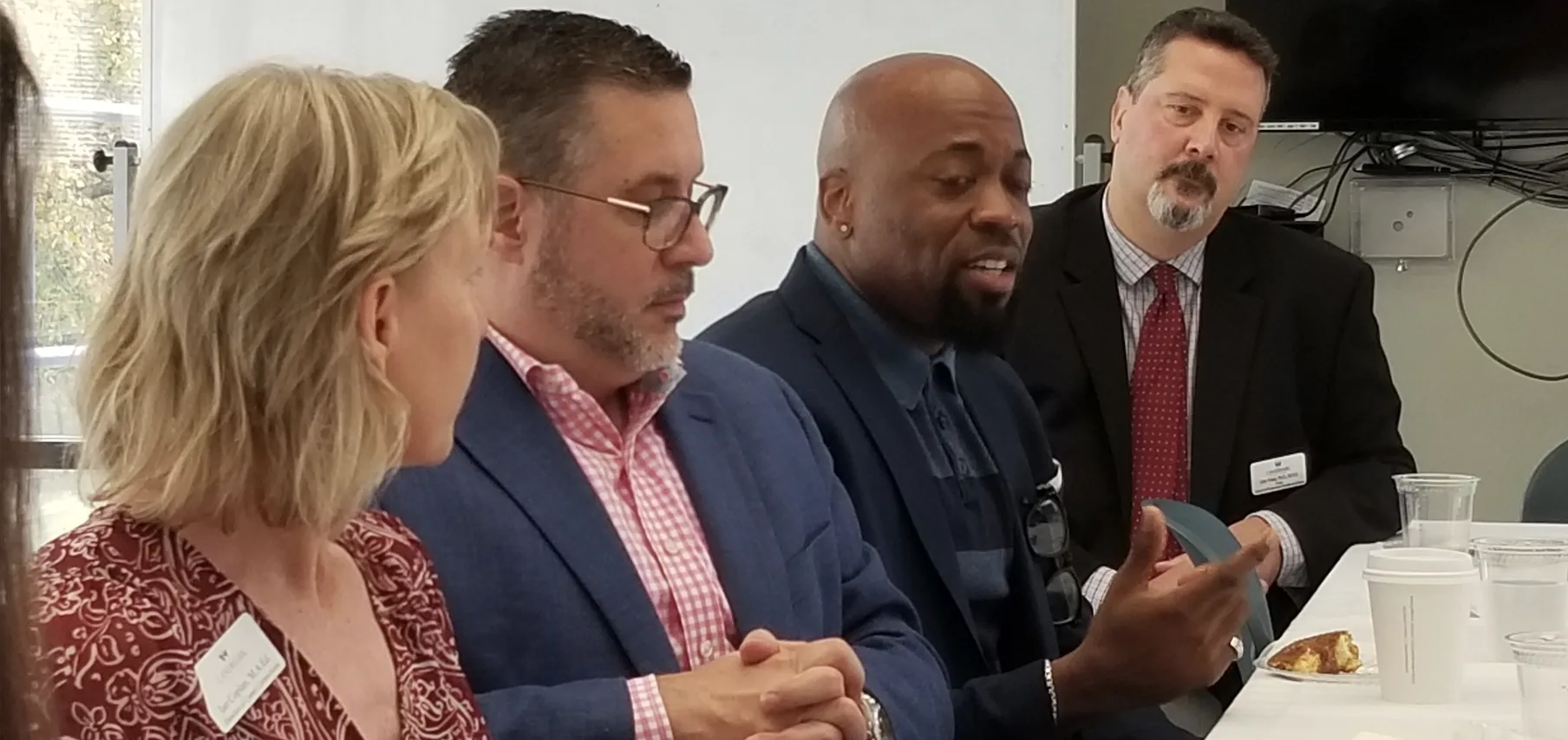 A group of four people engaged in discussion at a meeting table with food and drinks.