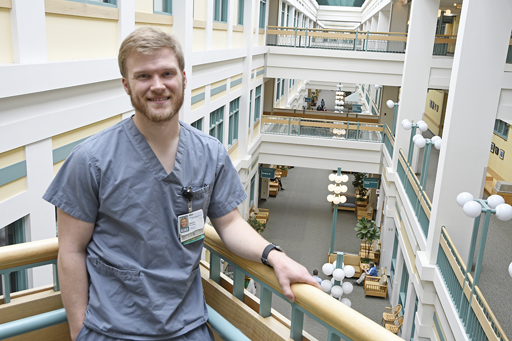 James Stockwell ’14 standing in scrubs on the second floor of Dartmouth Hitchcock's Medical Center atrium.