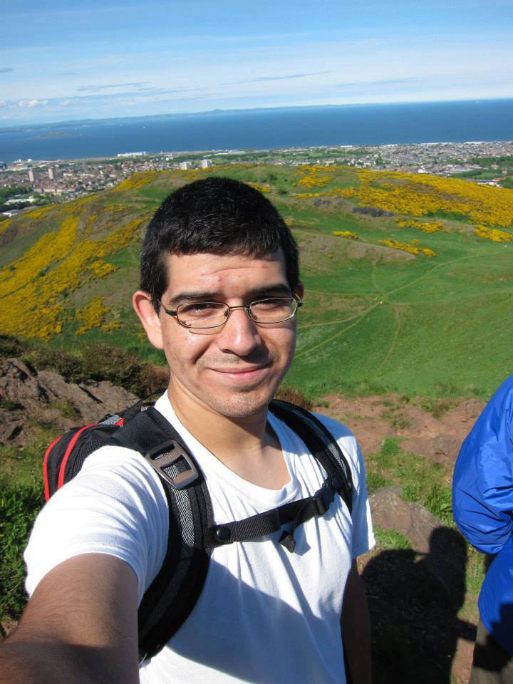 Selfie by Ben Lachman with ocean and green hill in background.