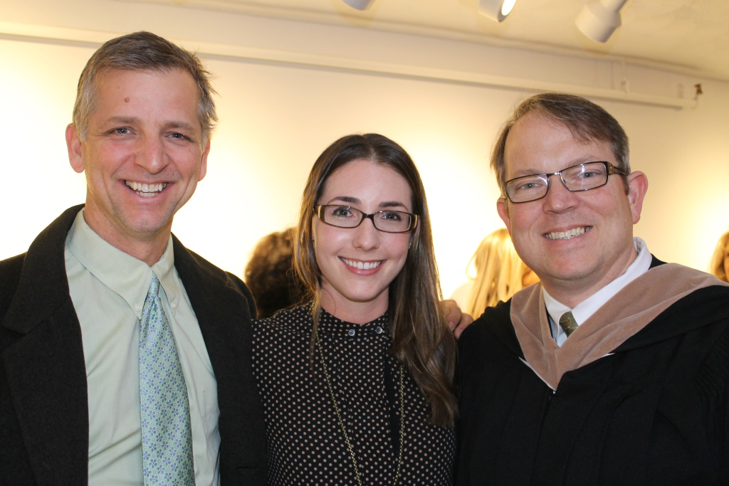Three people smiling indoors, with one wearing a suit, another in a dotted top, and the third in a formal robe.