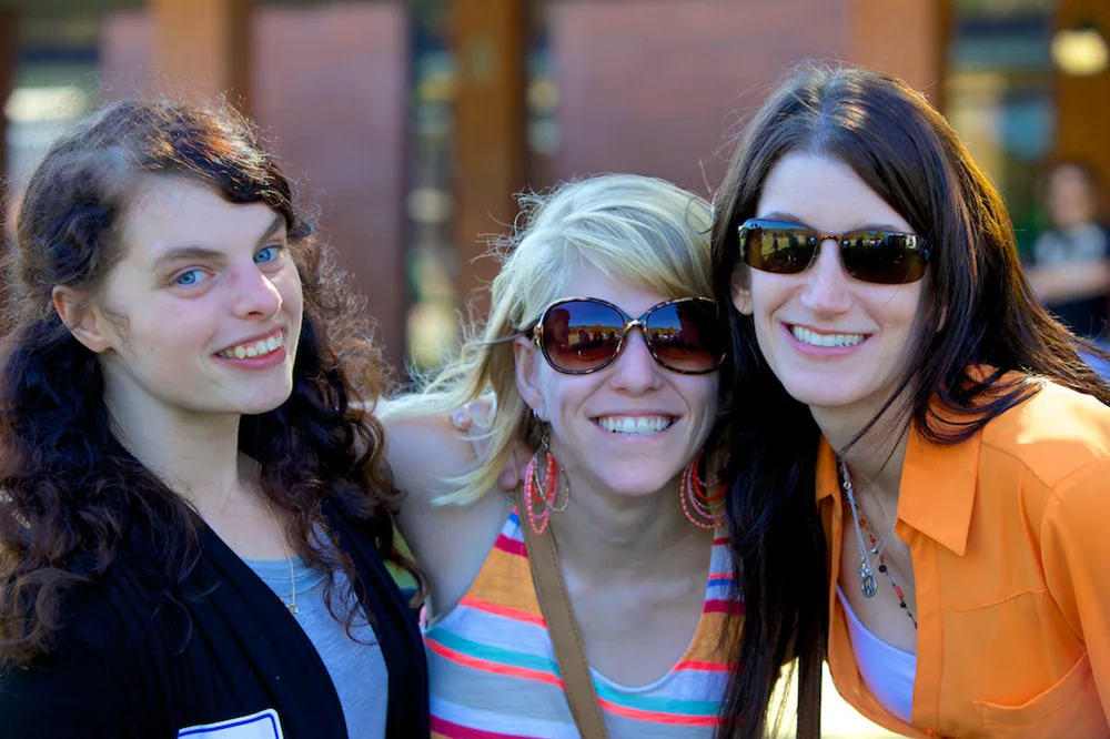 Three people smiling outdoors, wearing casual summer clothing and sunglasses.