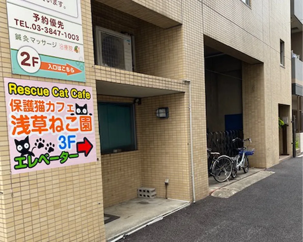 A picture of a brown building, there’s a sign in Japanese indicating the entrance to the cat cafe.