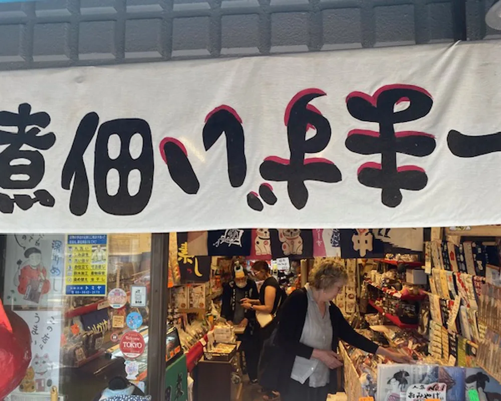Two professors browsing a gift shop, with part of a handwritten sign posted above the entrance in Japanese.