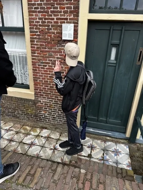 A person facing away from the viewer studies a plaque next to the door of a brick building.