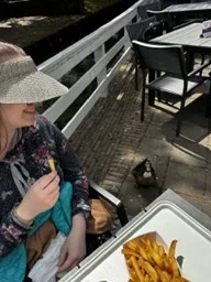A student eating french fries at a table, looks down at a duck who is on the ground looking up towards the fries.
