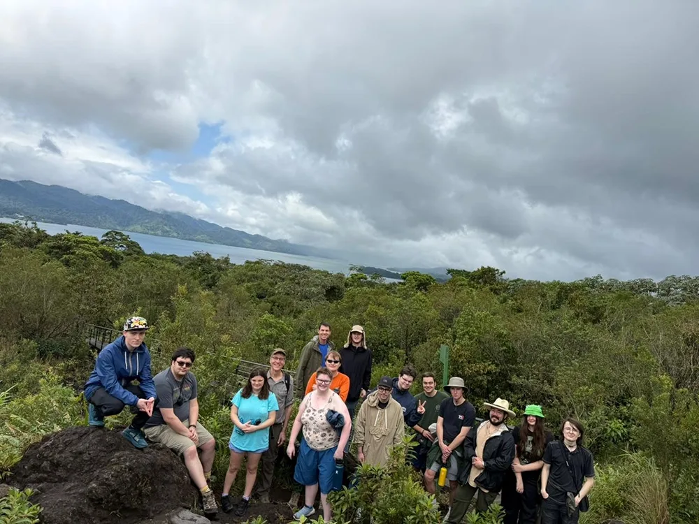 Students and trip leaders pose for a photo on rock with a view of a lake and mountains in the distance.
