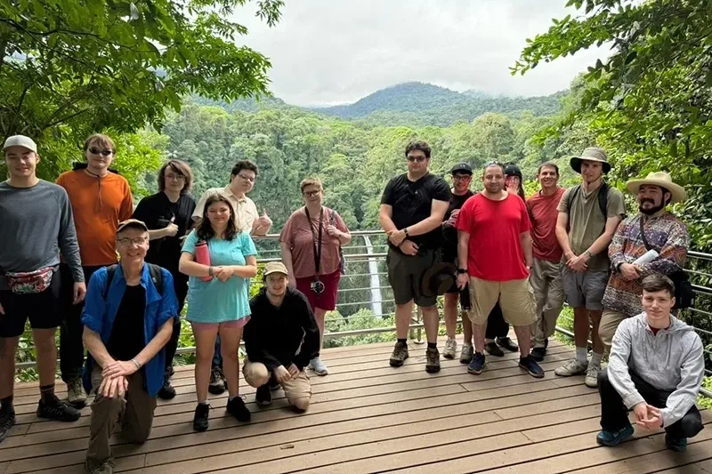 A group of people pose for a photo on a deck that looks out toward a waterfall.