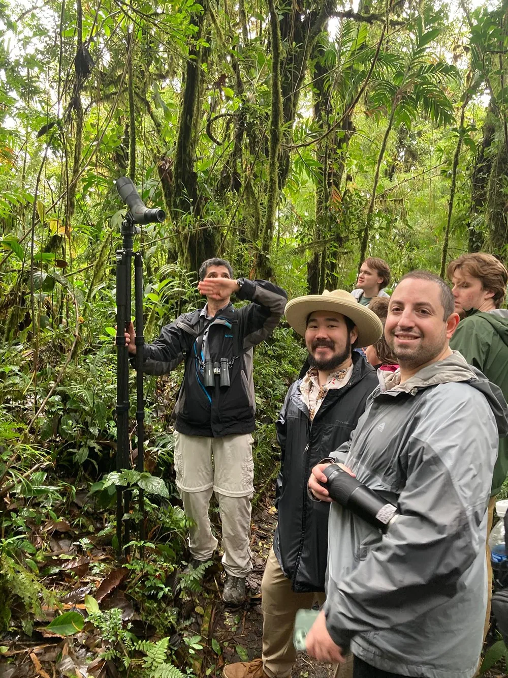 Two students smile at the camera amid the lush plant life of Manuel Antonio National Forest, Costa Rica. Another person stand behind them holding a camera on a tall tripod.