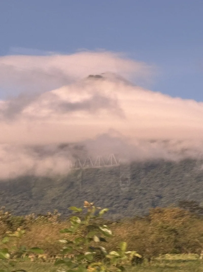 Distant view of volcano shrouded in heavy white clouds.