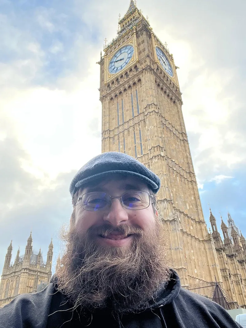 Student in hat and glasses in front of a tall clock tower