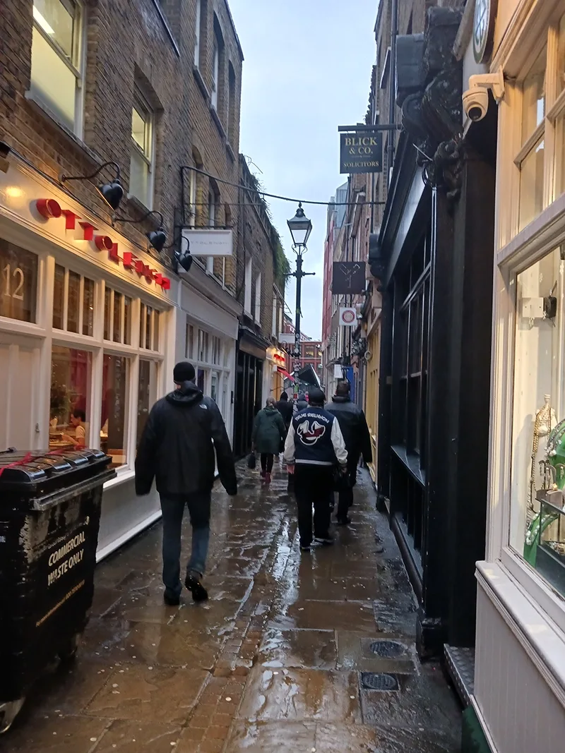 Group of students walking away from camera down a narrow alleyway on a rainy day