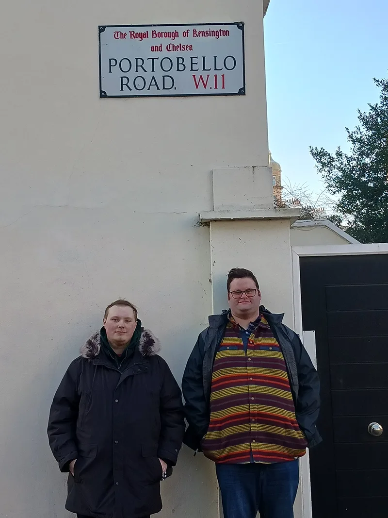 Two young men in winter jackets stand beneath a Portobello Road sign in Notting Hill, west London