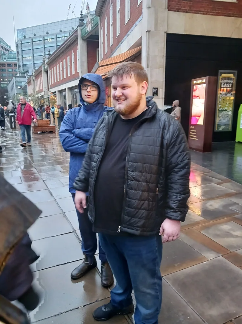Student in black winter jacket smiles as he looks at something off camera on a rainy sidewalk