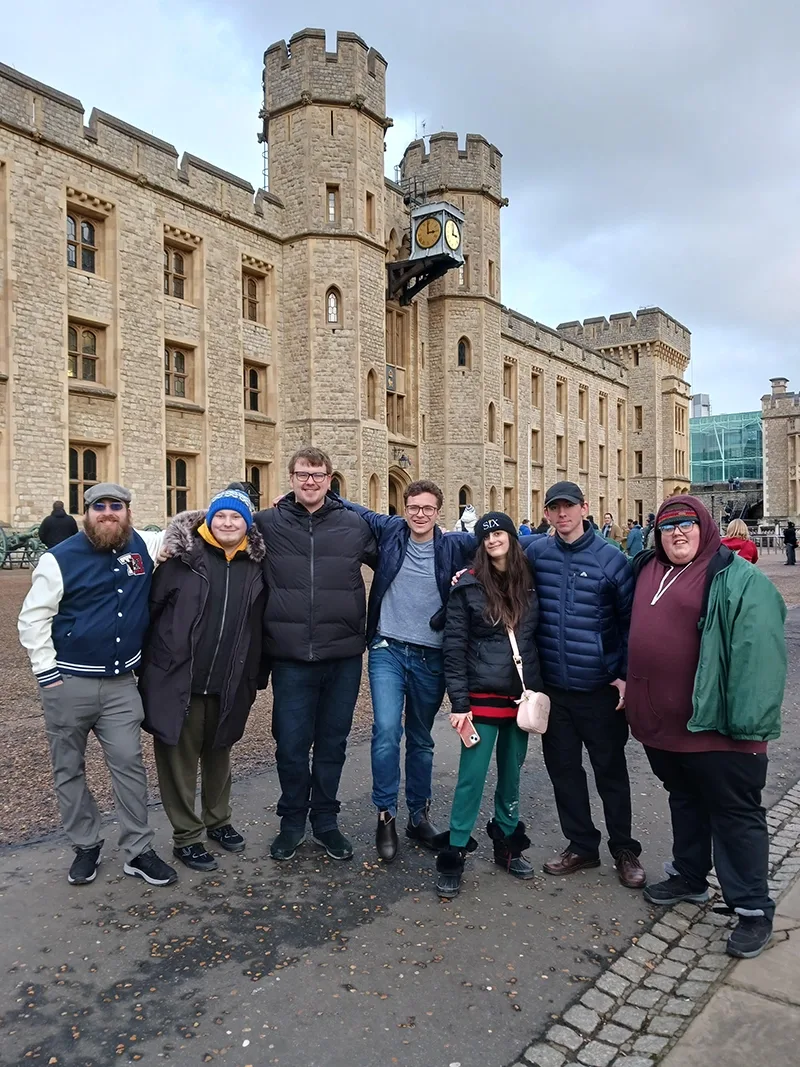 Six young men and a young woman stand shoulder to shoulder on the grounds of a historic palace: The Tower of London.