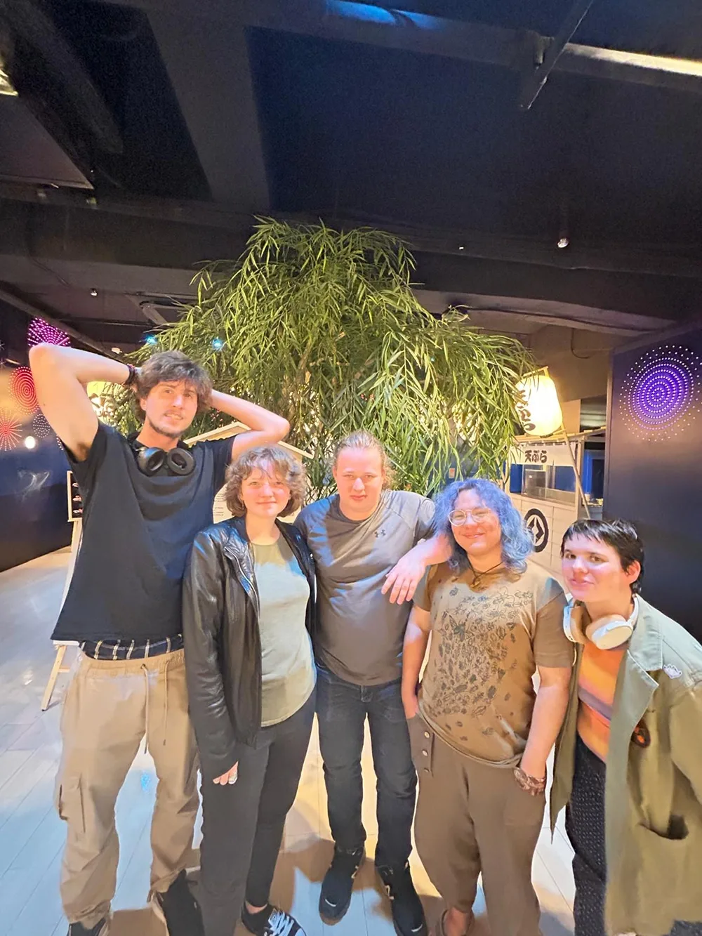Five people standing in front of large potted tree inside a room with glowing wall decorations