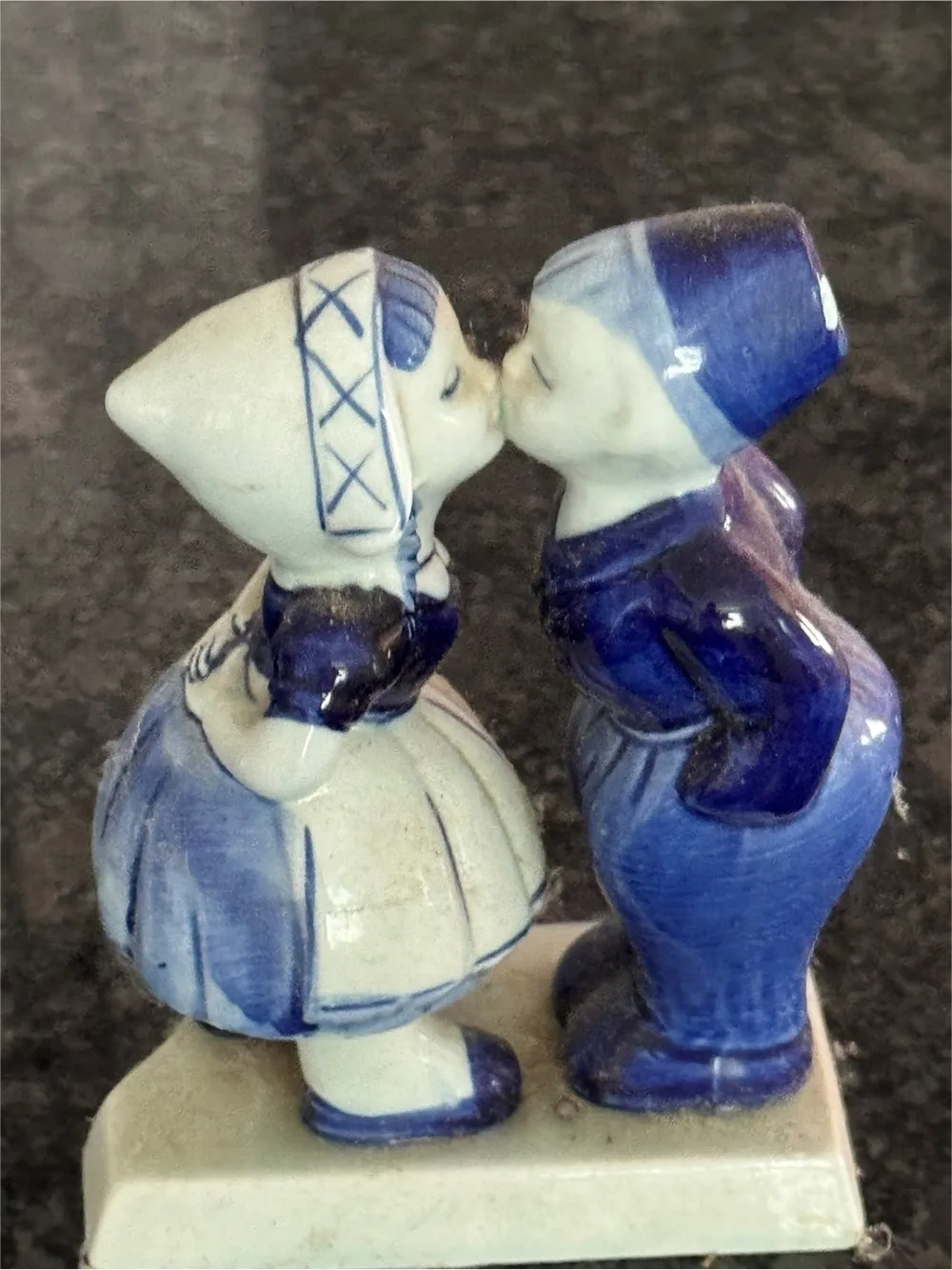 Image of small blue and white porcelain statuette of a young boy and girl dressed in traditional dutch garb leaning to eachother for a kiss.