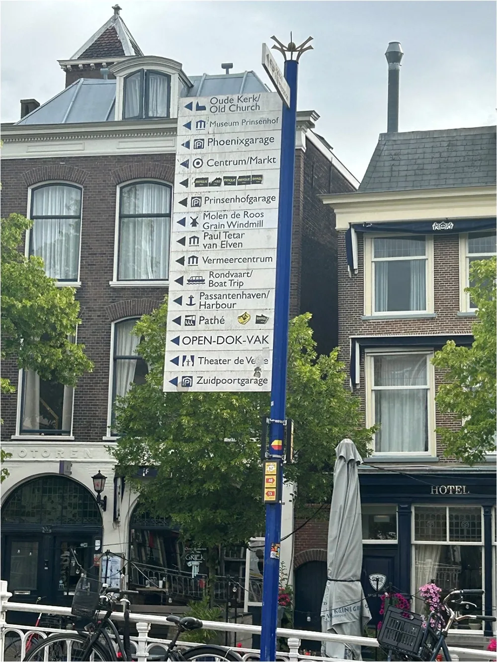 Photo of sign post with list of destinations and arrows pointing in the way. Backdrop of brick buildings on street.