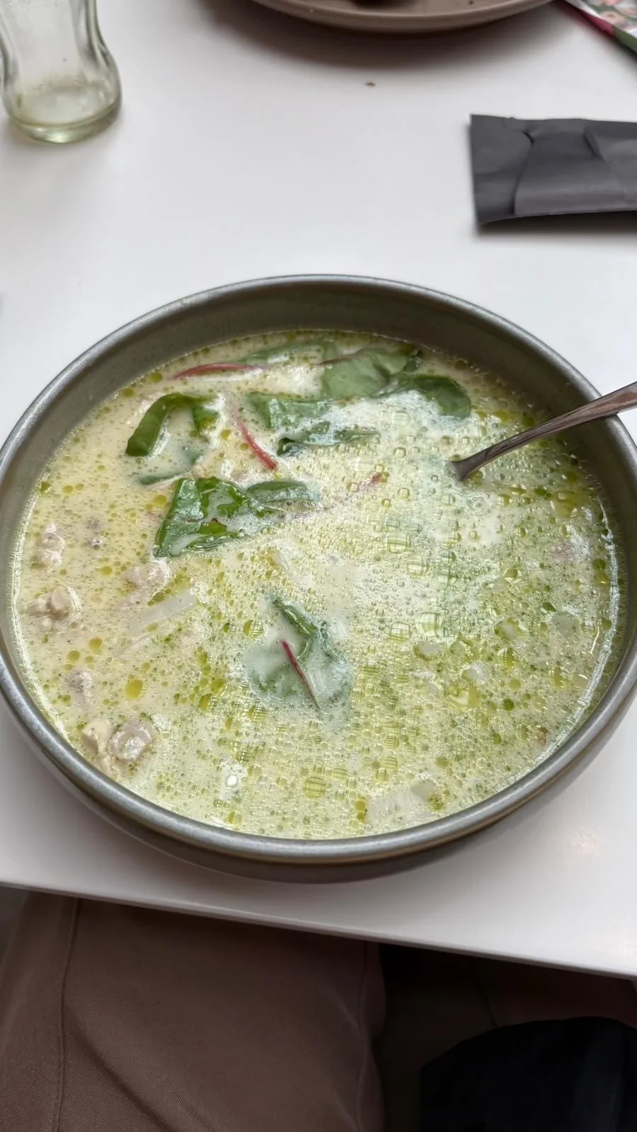 On a table top, a grey pottery bowl of creamy looking soup with leafy greens mixed in.