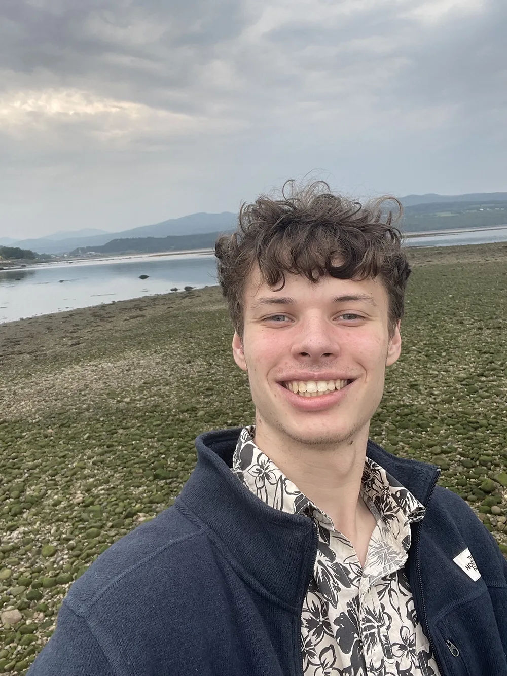 a picture of a student grinning with a view of a coastline in the background
