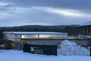 Exterior of Upper Campus Commons at dusk with temporary interior lighting visible through poly wrap
