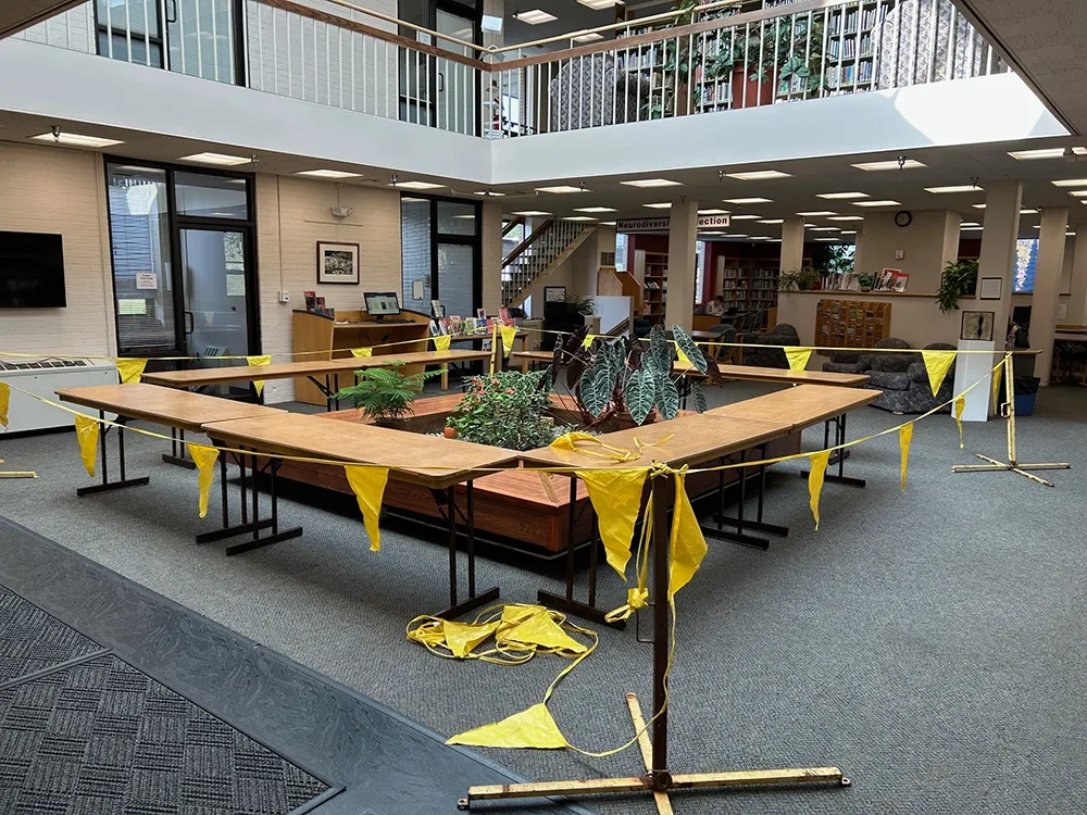 Yellow flags and ropes around a large squar coffee table-style structure with plantings in the center