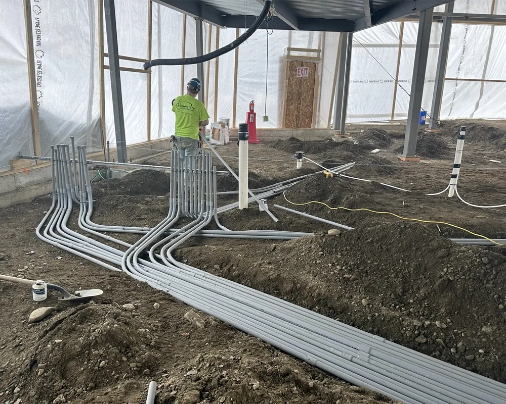 several long pieces of conduit piping with a construction worker laying it into dirt floor