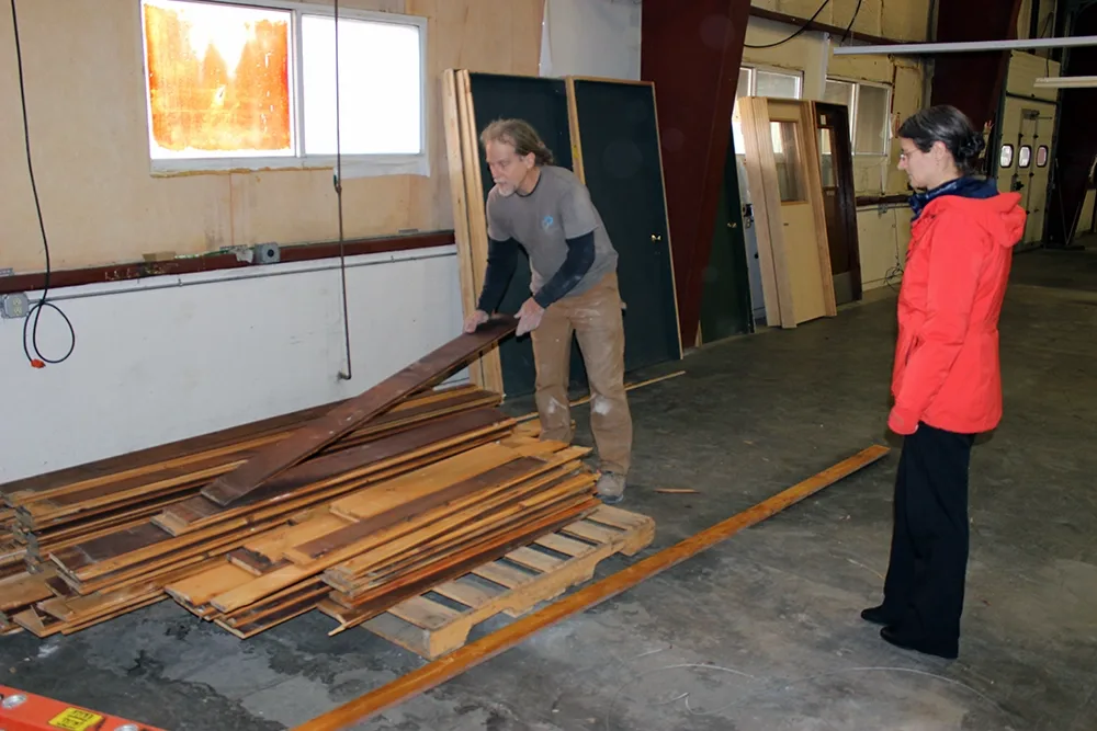 man lifting up a piece of wooden siding from the top of a large pile