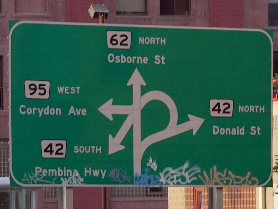 The infamous confusion corner street sign in Winnipeg. The sign shows four arrows crossing one another, each points to a different road.