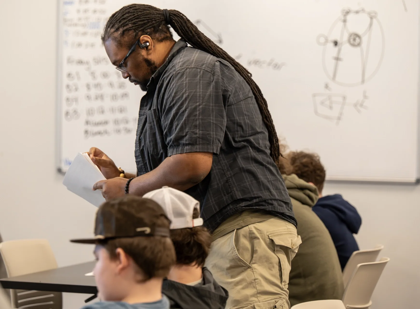 Student standing and writing notes on a piece of paper in a classroom.