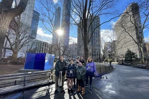 Student posing for picture in front of a large blue sculpture located in a park in downtown New York City.