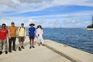 four students and a faculty member standing at the edge of a pier with several boats in the distant background