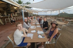 A large group of people sitting at a long table on an a restaurant patio deck