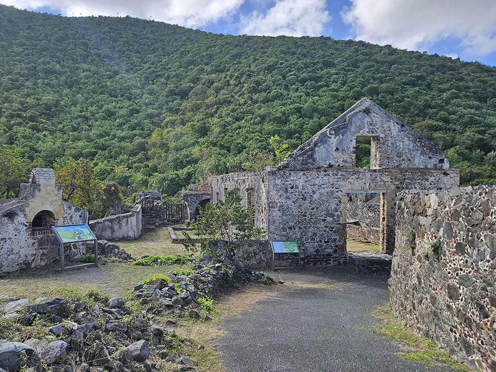 several stone structures and walls with a green hillside behind