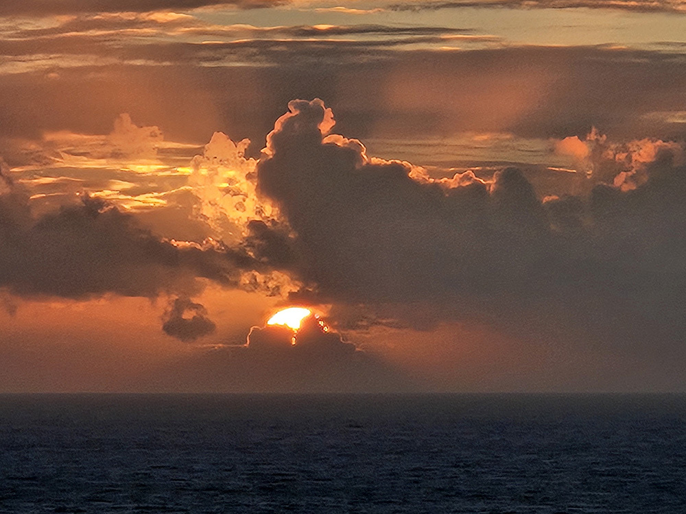 Sunride peeking through dark clouds over calm seawater