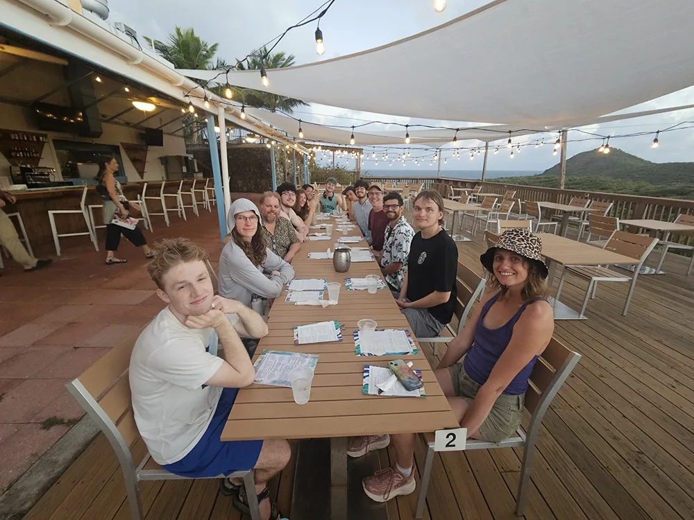 A large group of people sitting at a long table on an a restaurant patio deck