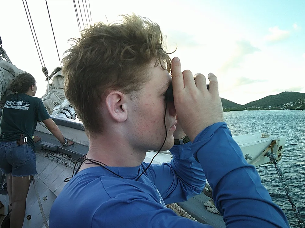 a student looking through binoculars out to the ocean from the deck of a ship