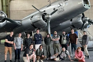 Group of students standing in front of an old-fashion plane in an airport hangar.