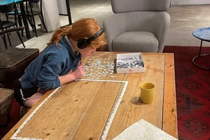 person with head phones leaning over a partially completed puzzle on a table.