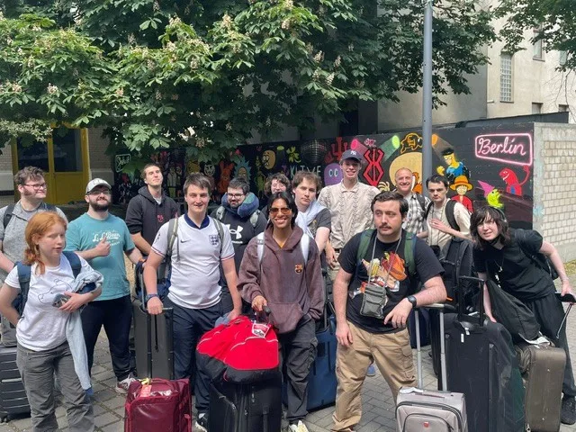 a group of students with their suitcases standing in a courtyard in front of wall with graffiti and the word Berlin.