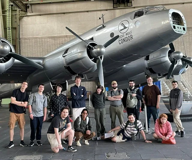 Group of students standing in front of an old-fashion plane in an airport hangar.