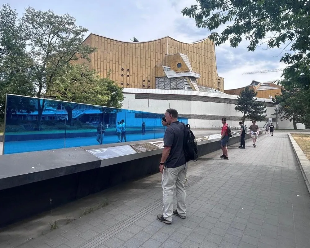 large, blue, glass wall with people walking around it.