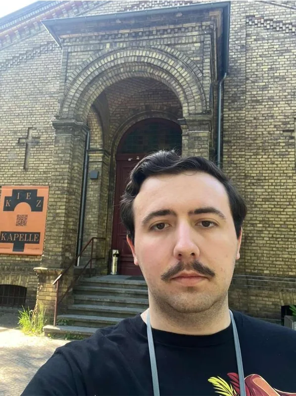 Somber person standing in front of the entrance way to a historical building with a cross