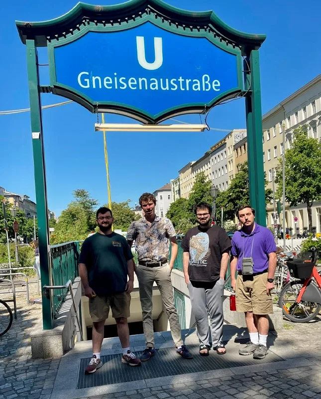 4 men standing in front of a sign at the entrance to the Berlin subway.