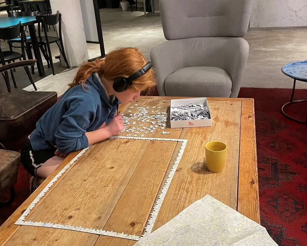 person with head phones leaning over a partially completed puzzle on a table.